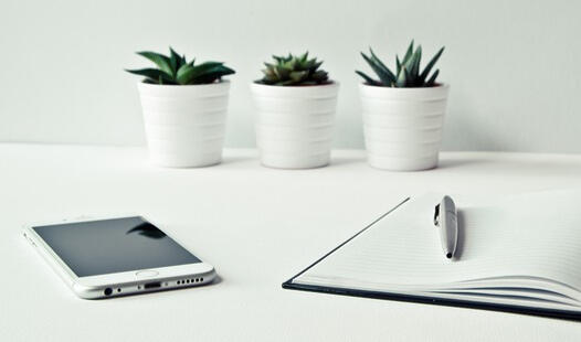 phone on desk White desk with phone, notebook & pen and three white pots with succulents